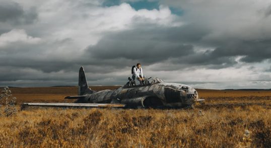 man on airplane wreck in grassland